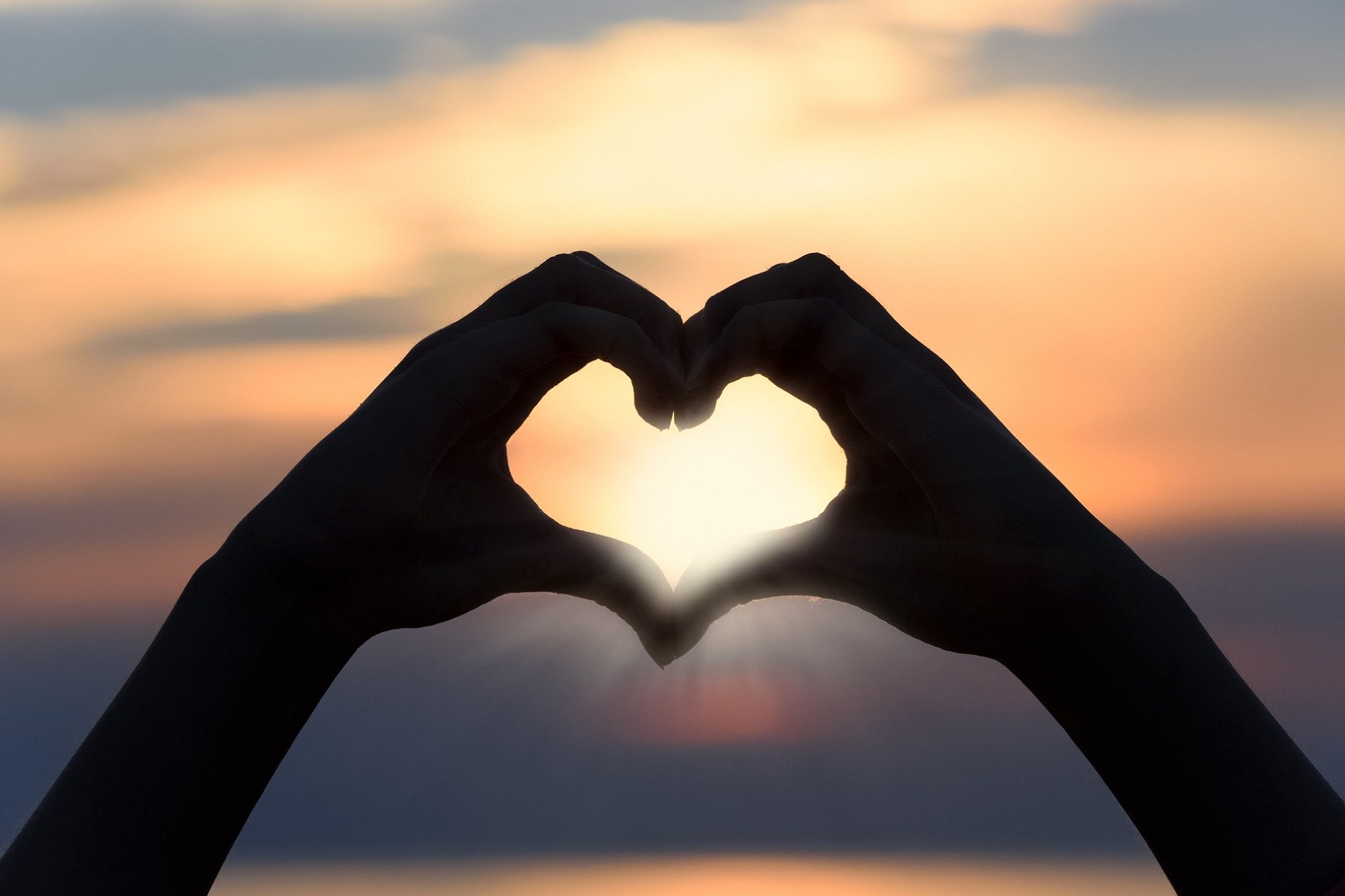 Mains en forme de coeur devant un coucher de soleil romantique